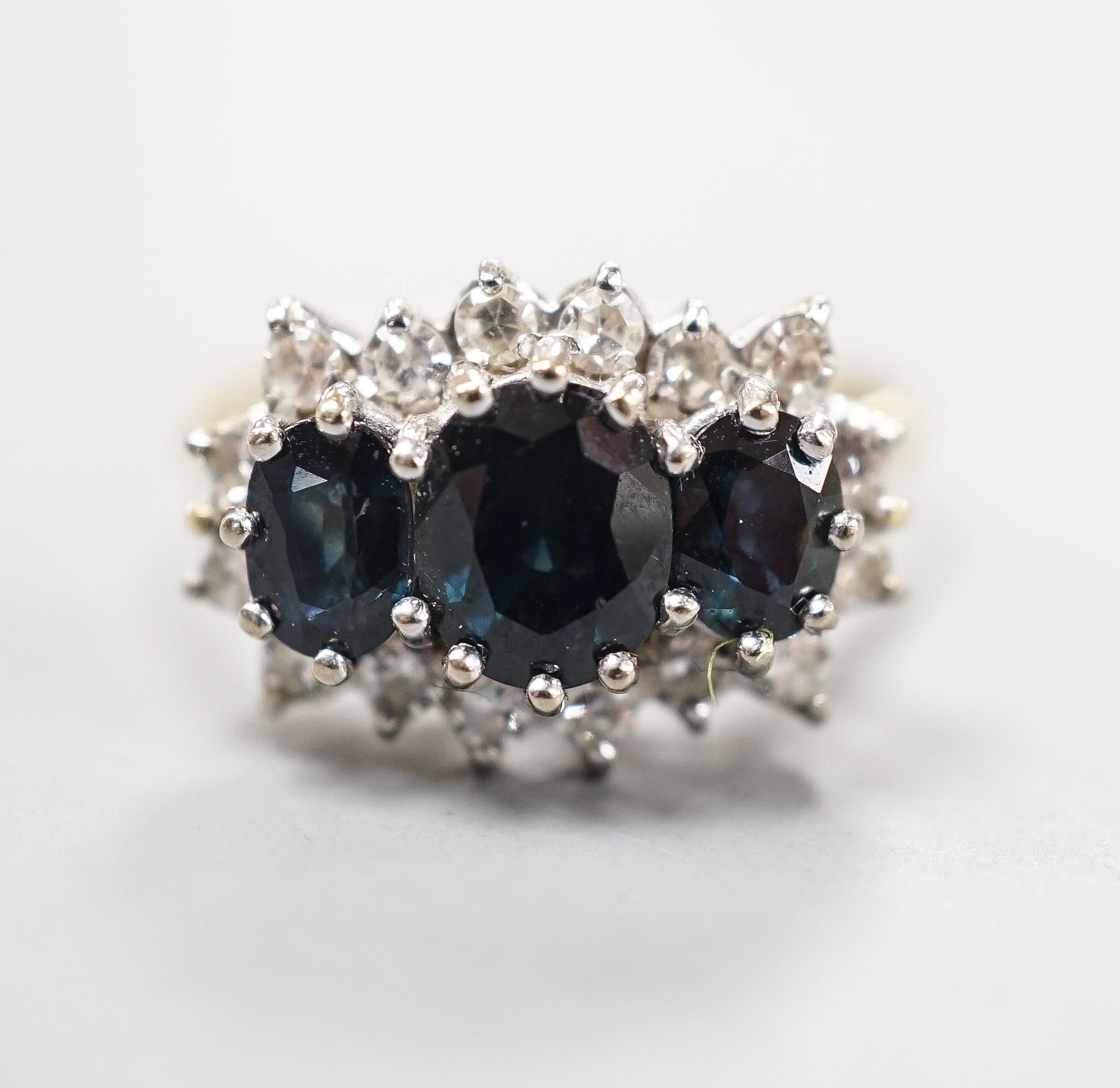 An 18ct and three stone sapphire set ring with diamond set border, size O, gross weight 5.3 grams.